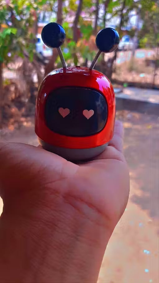 Mini Robot Car Perfume-Small red robot toy held in a hand with a blurred outdoor background
