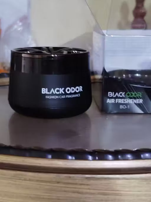 Black odor air freshener container on a reflective surface with a blurred background