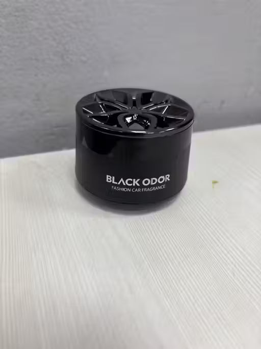 Black odor car fragrance device on a white surface with a gray background