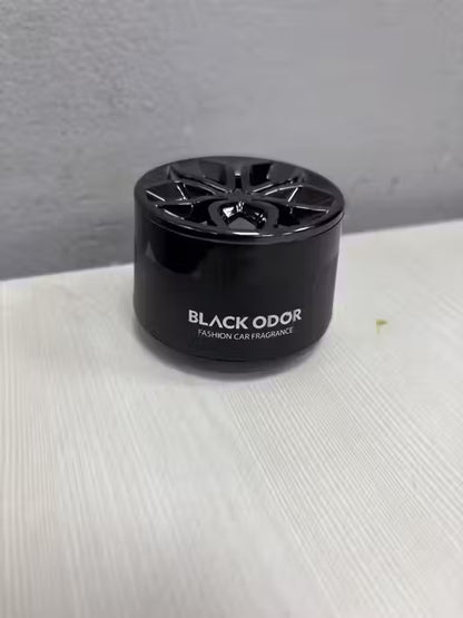 Black odor car fragrance device on a white surface with a gray background