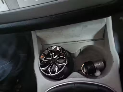 Car cup holder with a black and silver car air freshener and a small container.