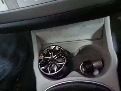 Car cup holder with a black and silver car air freshener and a small container.