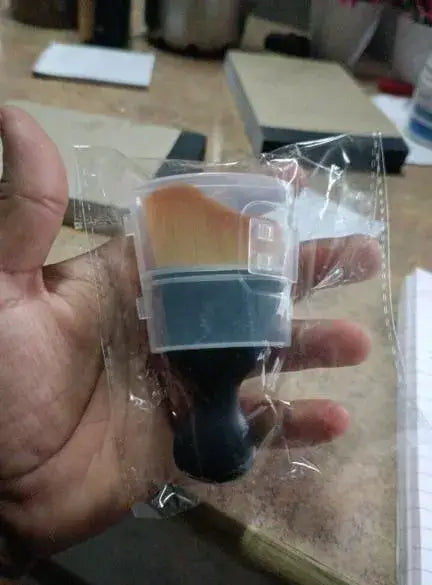 Best Car Dust Brush-Hand holding a small plastic container with a brush inside, on a blurred background.