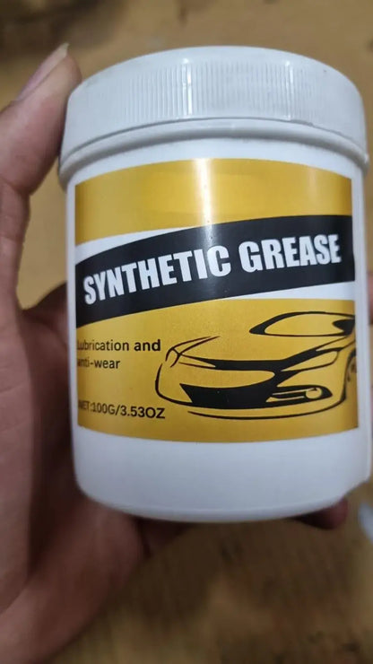 Container of synthetic grease held by a hand on a wooden surface