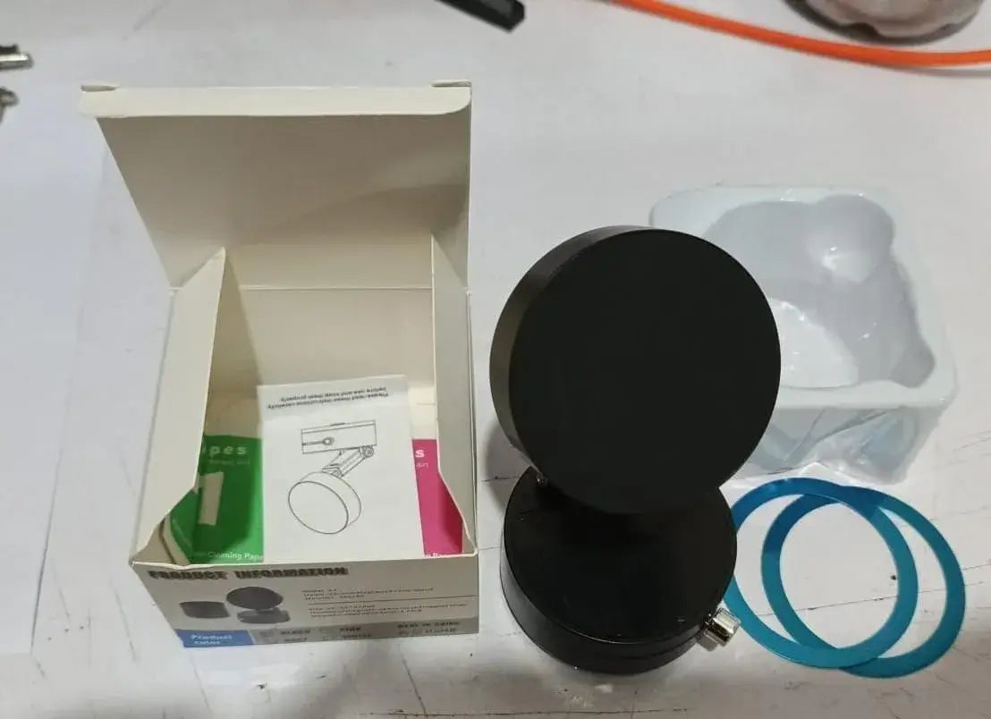 Black circular object on a white surface with a box and packaging materials in the background.