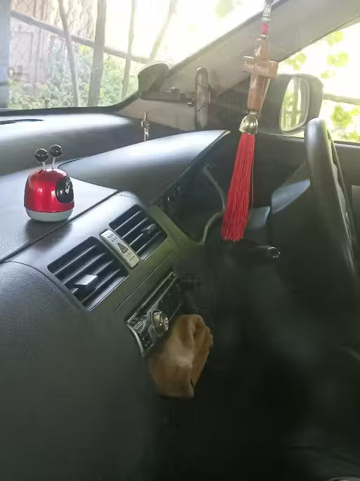 Mini Robot Car Perfume-Car dashboard with a red car accessory and tassel hanging from the rearview mirror.