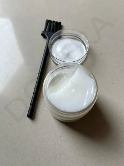 Two containers of white cream with a black brush on a beige surface